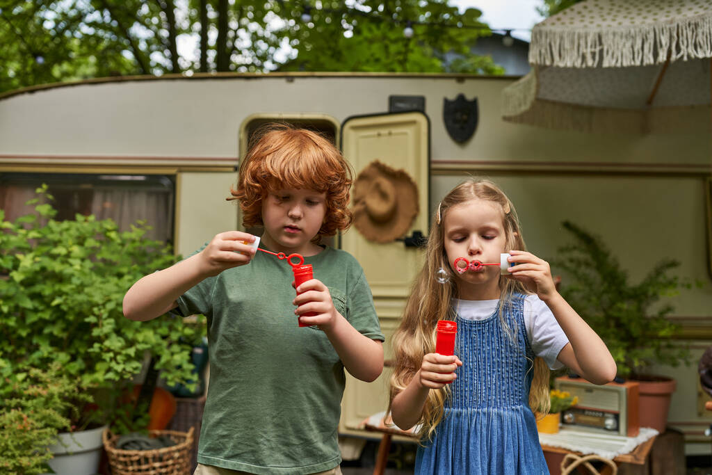 zrzka chlapec a blondýny dívka foukání mýdlo bubliny v blízkosti přívěsu domů, sourozenci hrát spolu - Fotografie, Obrázek