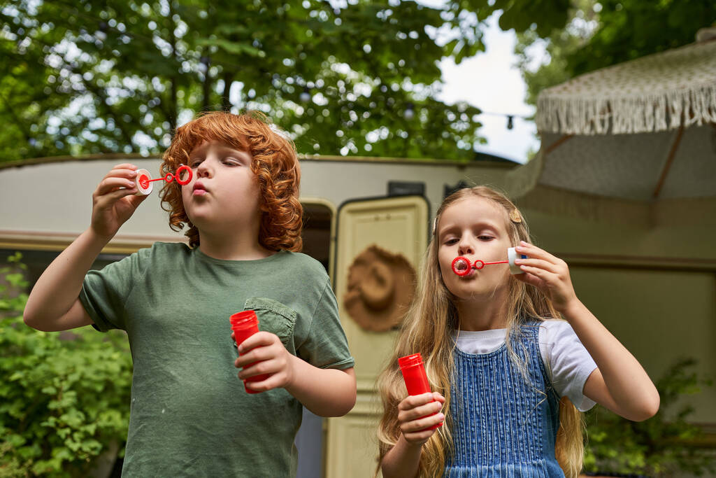 Рыжий брат и блондинка сестра раздувая мыльные пузыри возле трейлера дома, брат и сестра - Фото, изображение