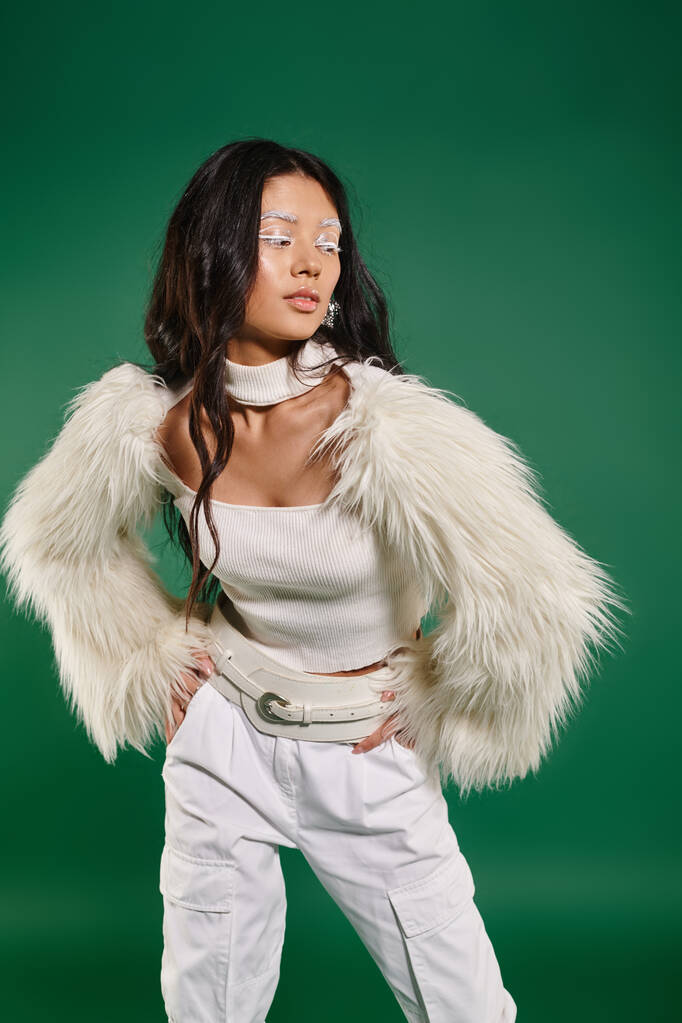 asian brunette woman in total white outfit and makeup posing with hands on hips on green backdrop - Photo, Image