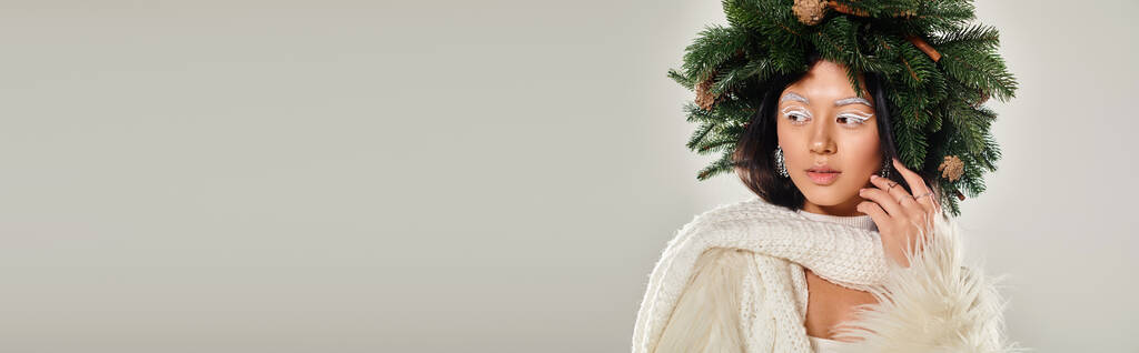 belleza de invierno, mujer atractiva con corona de pino natural posando en ropa blanca en gris, bandera - Foto, Imagen