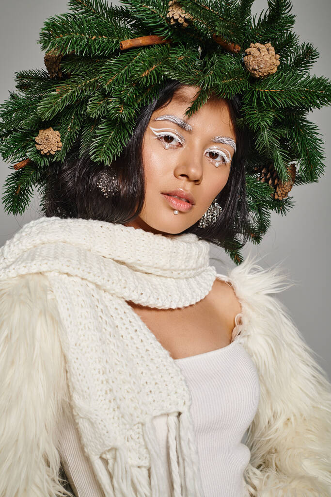 beautiful winter queen with white eye makeup and beads on face posing in wreath on grey background - Photo, Image