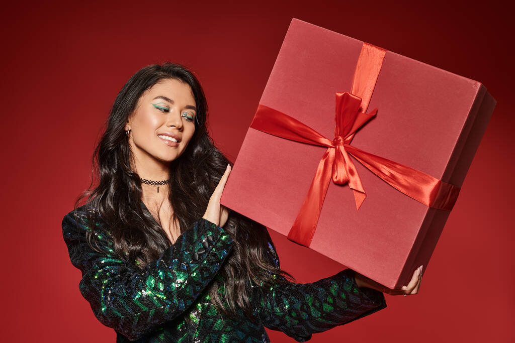 happy asian woman in green jacket with sequins holding present on red backdrop, Merry Christmas - Photo, Image