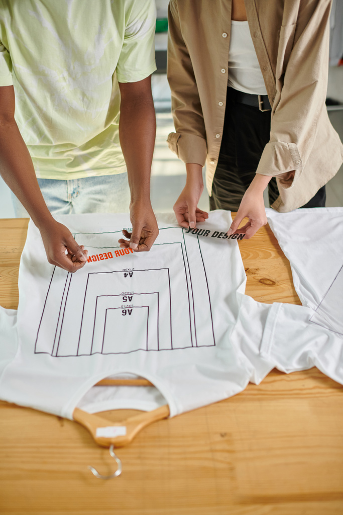 vista recortada de diseñadores interracial sosteniendo plantillas de texto cerca de camisetas con tamaños de formato - Foto, Imagen