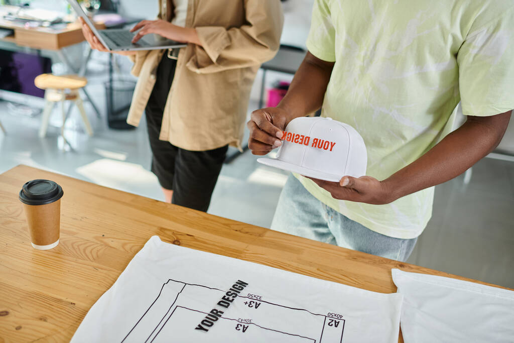 обрізаний вид афроамериканського дизайнера з шапкою і текстовим шаблоном біля колеги з ноутбуком - Фото, зображення