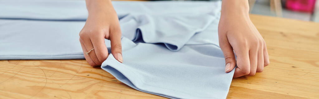 bijgesneden weergave van ijverige vrouw werken in textiel print workshop tijdens het vouwen van kleding, banner - Foto, afbeelding