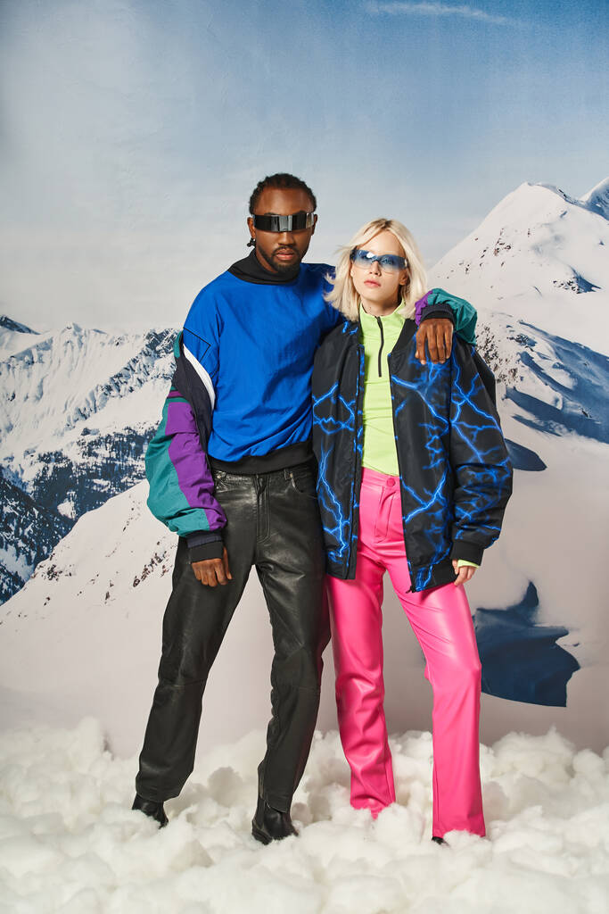 stylisches multiethnisches Paar, das sich umarmt und vor verschneiter Bergkulisse posiert, Winterkonzept - Foto, Bild