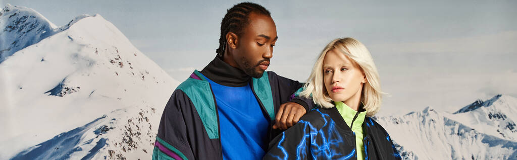 elegante coppia multiculturale in abiti audaci con montagna innevata sullo sfondo, concetto invernale, banner - Foto, immagini