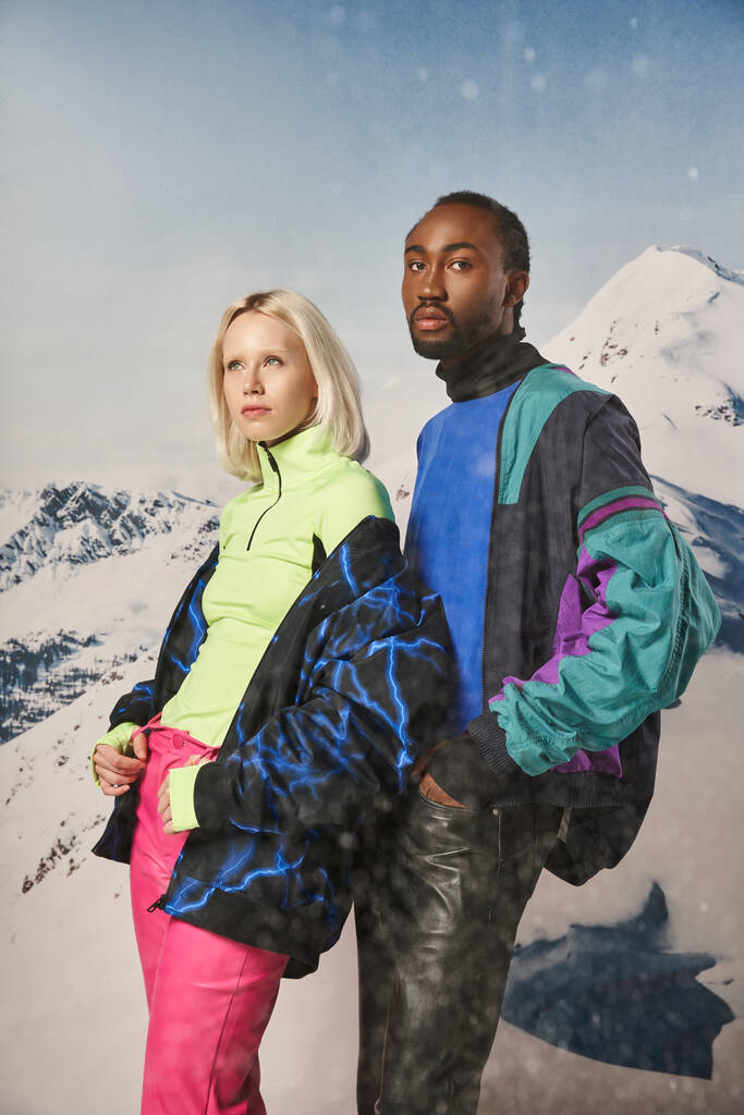 attraktives vielseitiges Paar in stylischen warmen Outfits mit schneebedecktem Berg vor der Kulisse, Winterkonzept - Foto, Bild
