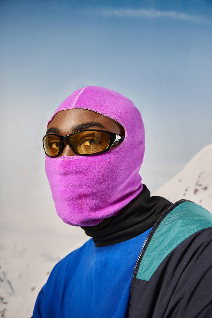junger afrikanisch-amerikanischer Mann in pinkfarbener Sturmhaube und Sonnenbrille blickt in die Kamera, Winterkonzept - Foto, Bild