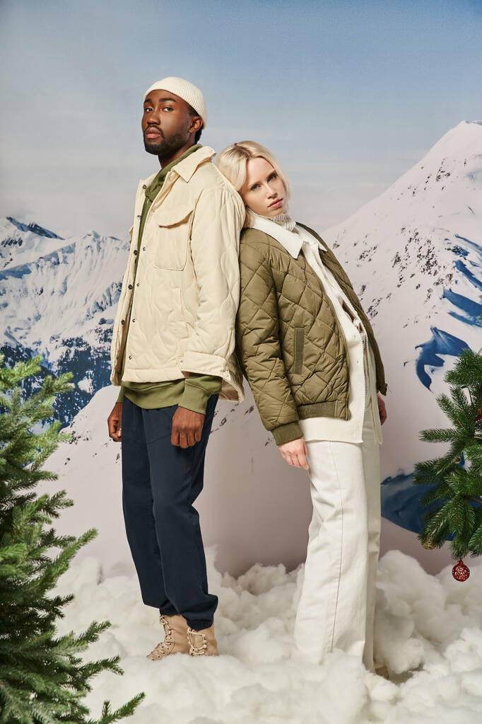ウィンタージャケットのスタイリッシュな多文化カップルは,木に合うように背中を向ける,冬のコンセプト - 写真・画像