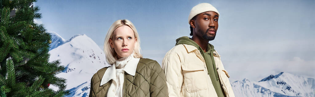 elegante pareja multiétnica en chaquetas de moda con telón de fondo de montaña, moda de invierno, bandera - Foto, Imagen