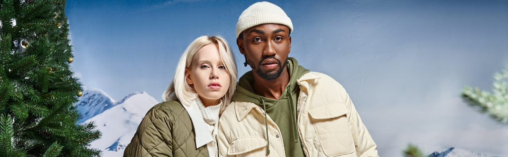 cute interracial couple in warm clothes posing together on snowy backdrop, winter fashion, banner - Photo, Image
