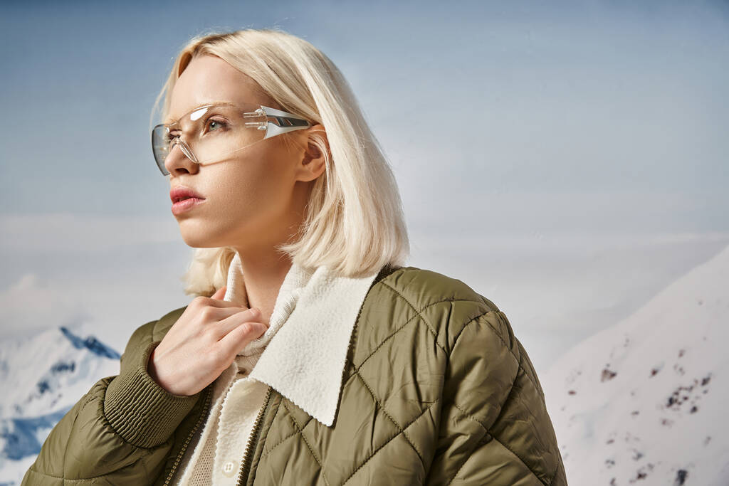 beautiful blonde woman in modish glasses wearing warm jacket and looking away, winter fashion - Photo, Image