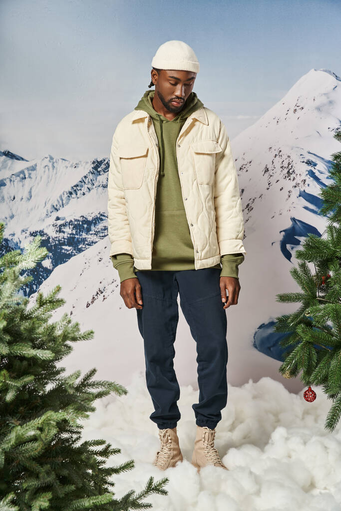 handsome african american man in beanie hat looking down with mountain backdrop, winter fashion - Photo, Image