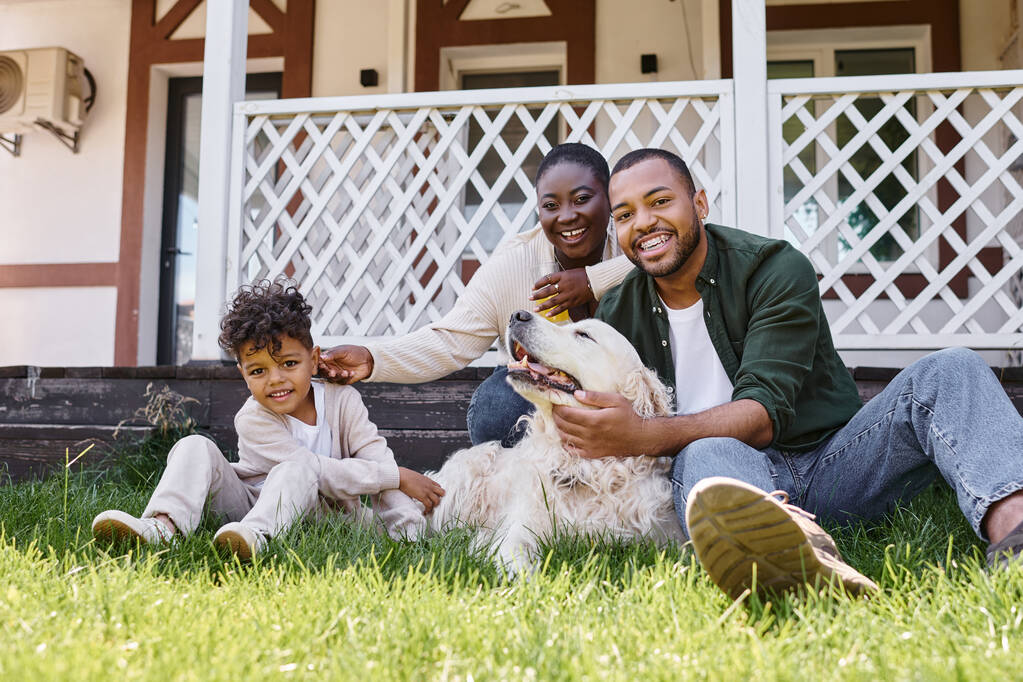 家族の時間,陽気なアフリカ系アメリカ人の両親とキュリーな息子は家の裏庭で犬と遊んでいます - 写真・画像