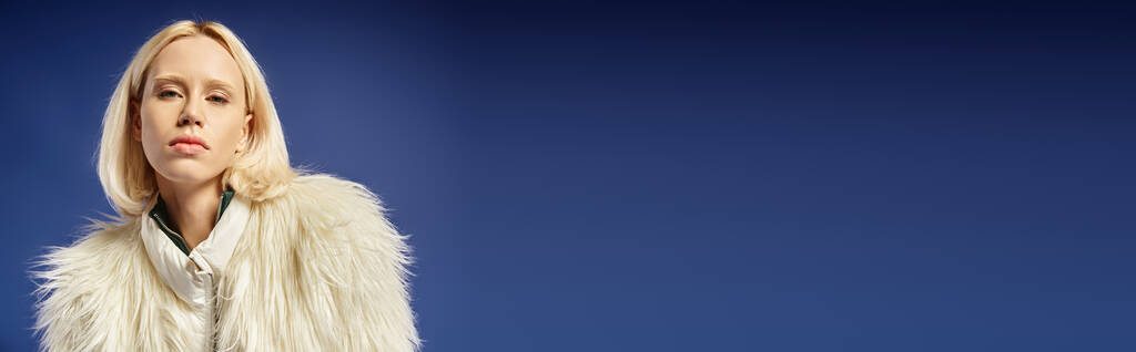 talvibanderolli, muotokuva nuoresta naisesta valkoisessa tekoturkistakissa katselemassa kameraa sinisellä taustalla - Valokuva, kuva