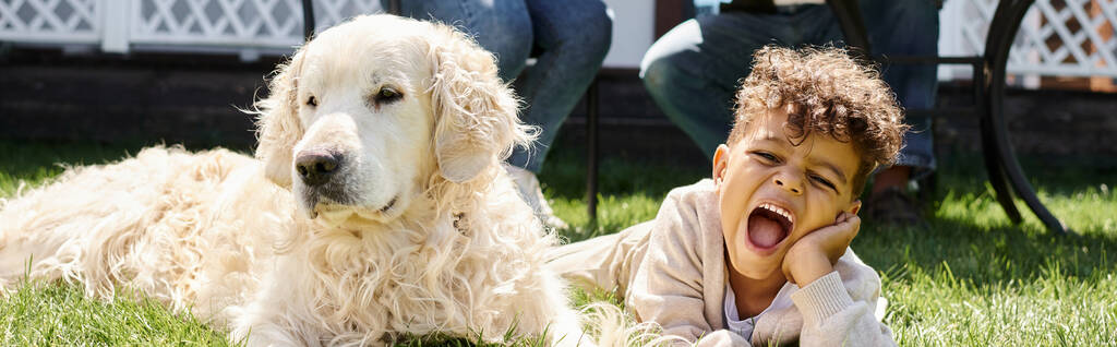 emotional african american boy lying on green lawn next to family dog on backyard, horizontal banner - Photo, Image