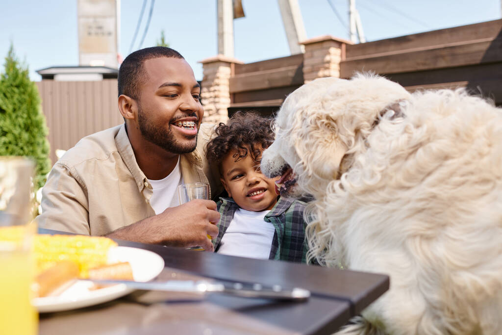 happy african american father and curly son petting dog during family bbq on backyard, family - Photo, Image