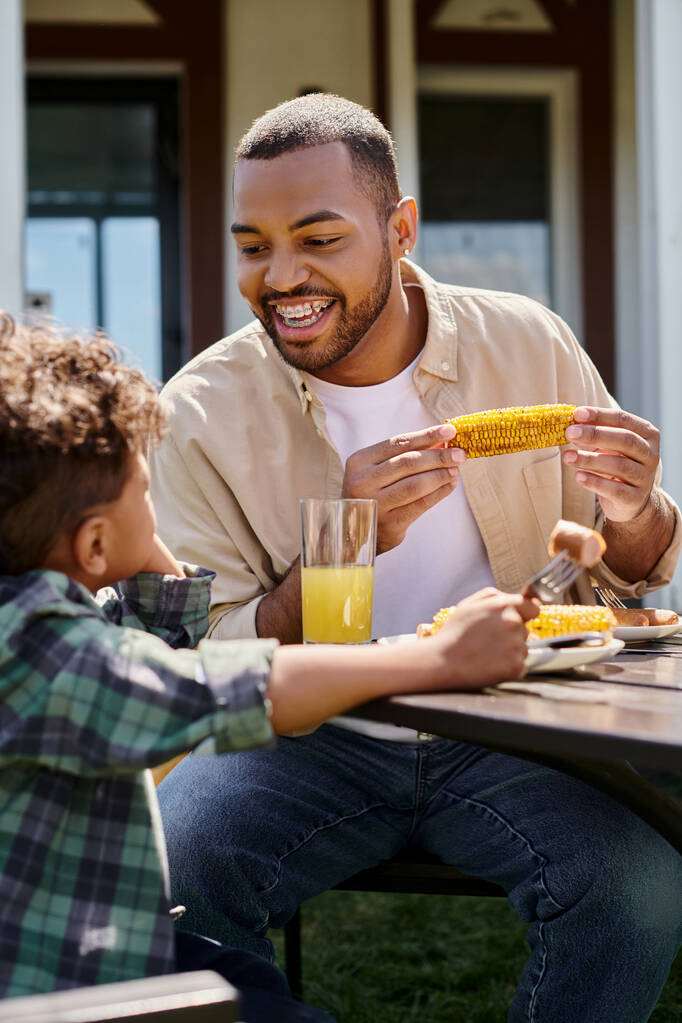 positive african american father having family bbq with curly son on backyard of house, grilled corn - Photo, Image