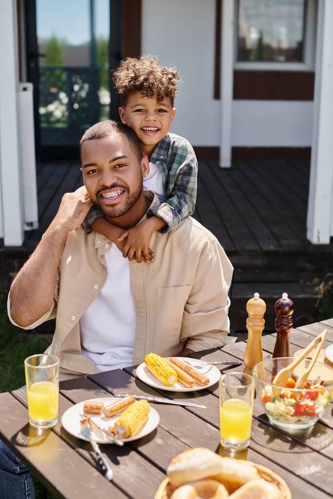 glücklich afrikanisch-amerikanisches Kind umarmt Vater beim Grillen im Hinterhof des Hauses, Familie - Foto, Bild