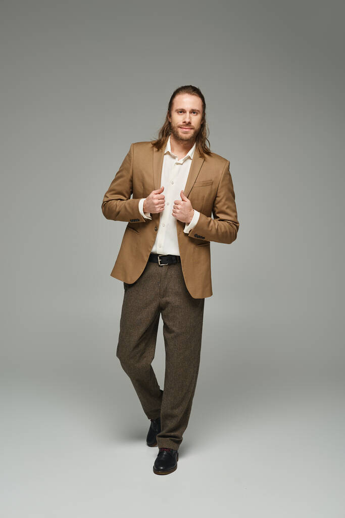 повна довжина бізнесмена з бородою і довгим волоссям позує на сірому тлі, формальний одяг - Фото, зображення