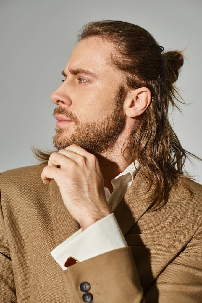 retrato de hombre de negocios guapo con pelo largo y barba posando en blazer beige sobre fondo gris - Foto, imagen