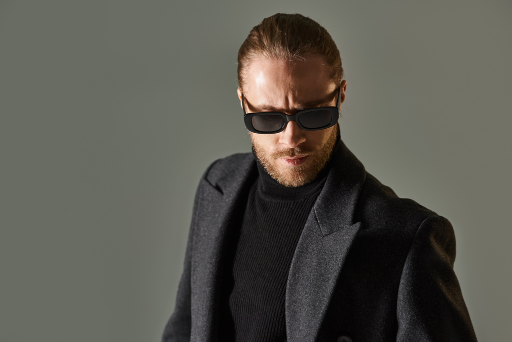 портрет красивого бородатого мужчины в модных солнцезащитных очках и черном одеянии, позирующего на сером фоне - Фото, изображение
