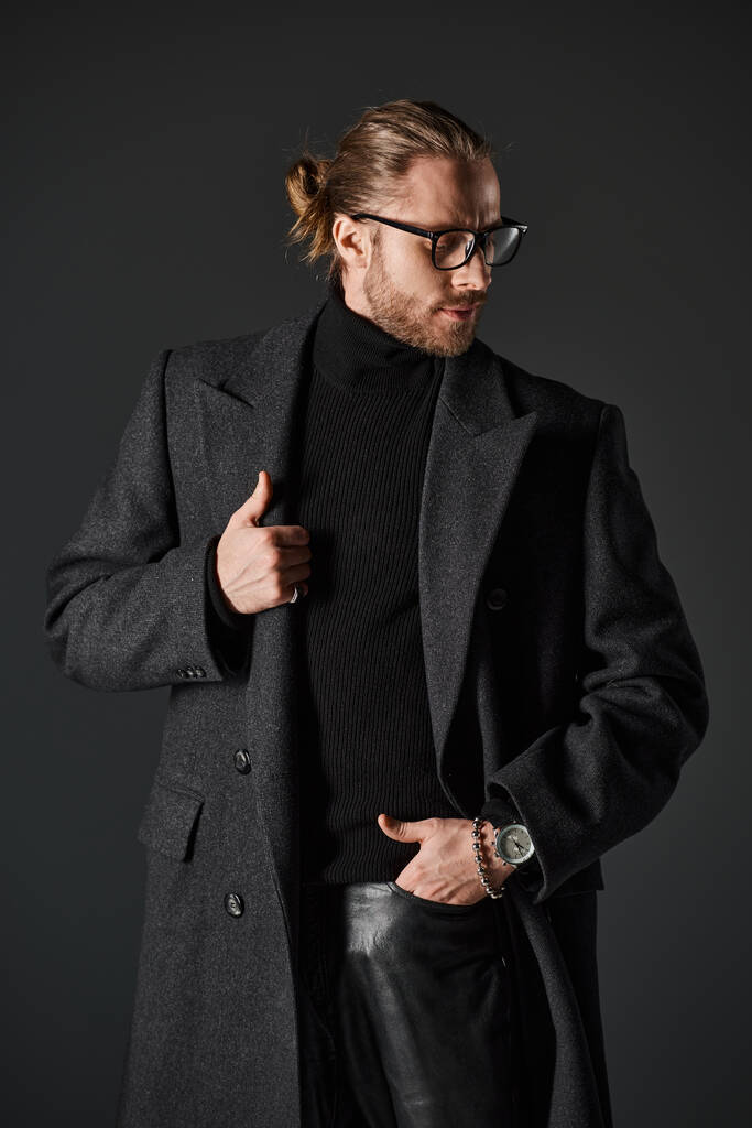 man met baard in bril en stijlvolle wollen jas poseren met de hand in zak op grijze achtergrond - Foto, afbeelding