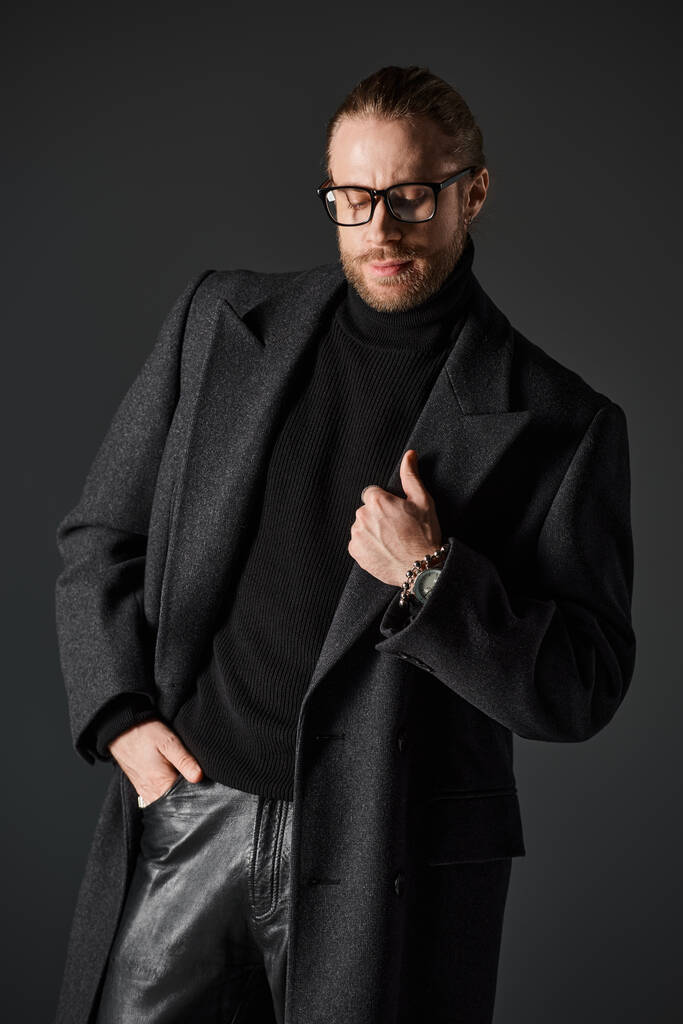przystojny mężczyzna w okularach i elegancki wełniany płaszcz pozowanie z ręką w kieszeni na szarym tle - Zdjęcie, obraz