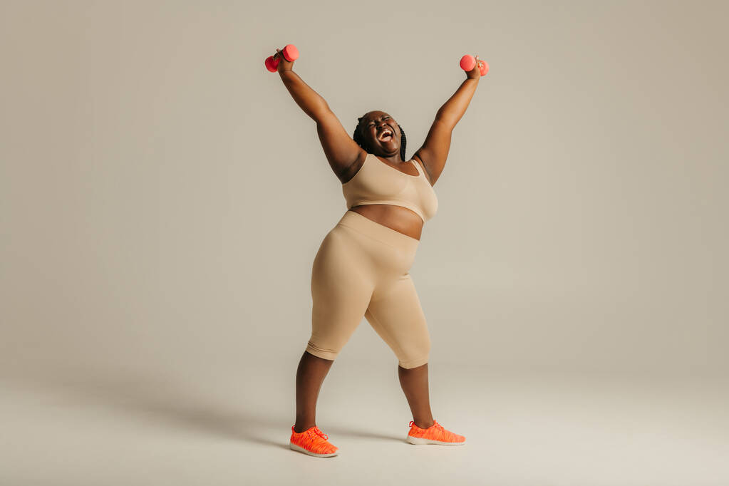 Pewność siebie plus rozmiar African kobieta w odzieży sportowej promieniujące zaufanie podczas ćwiczeń na tle studio - Zdjęcie, obraz