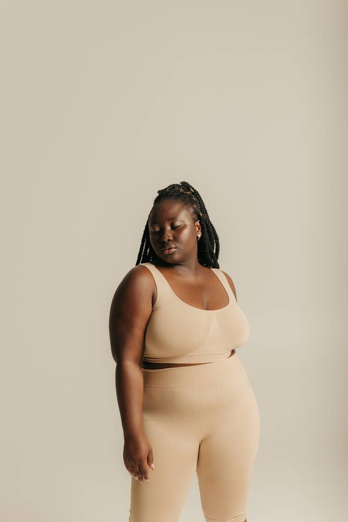 Красивая африканка плюс размер женщины в нижнем белье излучающей самолюбие, стоя на студийном фоне - Фото, изображение