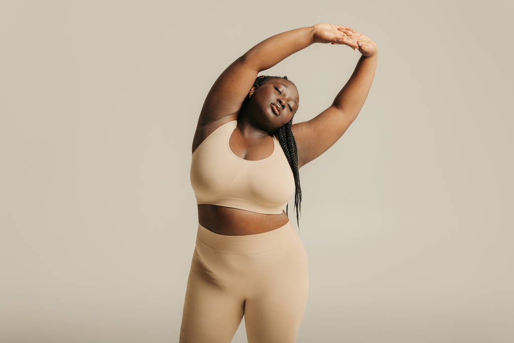 Atractiva mujer africana de talla grande en ropa interior que irradia amor propio mientras está de pie en el fondo del estudio - Foto, imagen