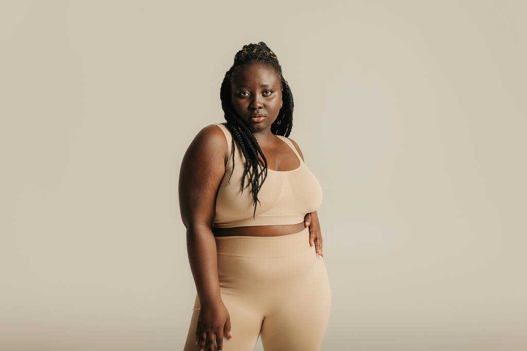 Krásná africký plus velikost žena ve spodním prádle hledá jistotu v jejím těle na pozadí studia - Fotografie, Obrázek