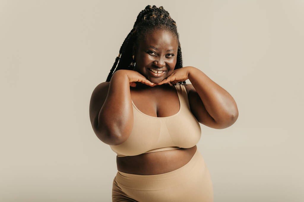 Mooie voluptueuze Afrikaanse vrouw in ondergoed aanraken gezicht en glimlachen op studio achtergrond - Foto, afbeelding