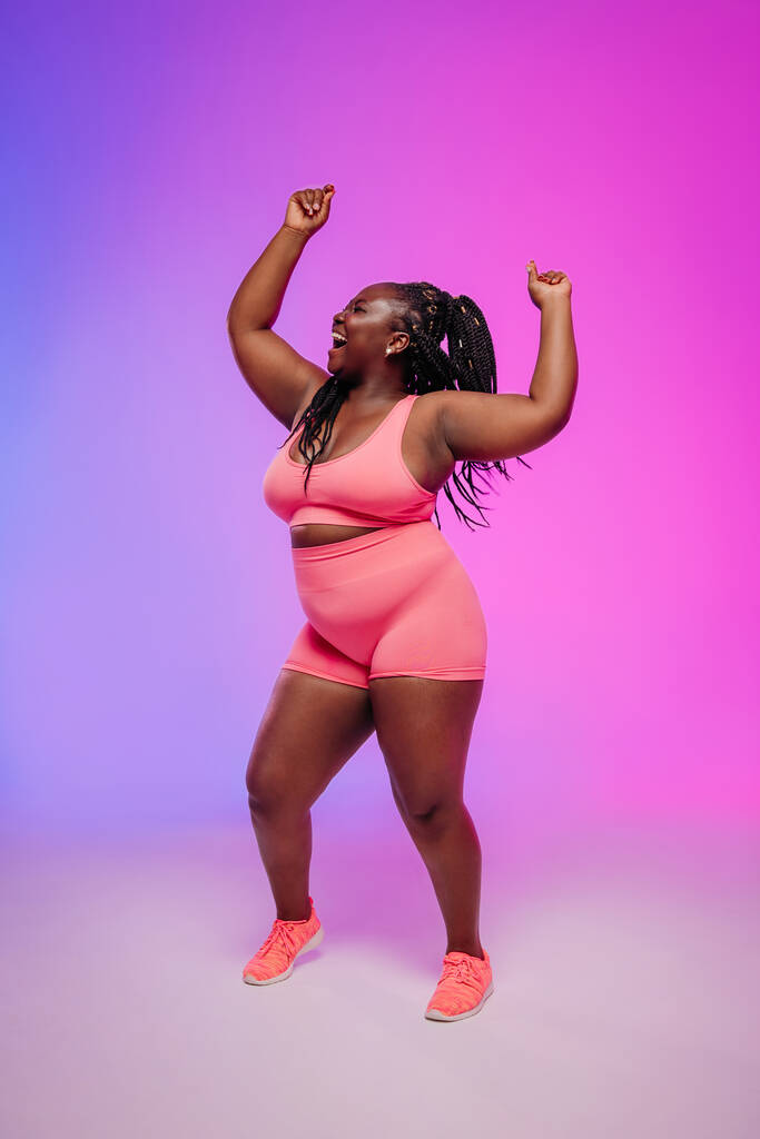 Happy African plus velikost žena ve sportovním oblečení těší tanec a hledá jistotu na pulzujícím pozadí - Fotografie, Obrázek