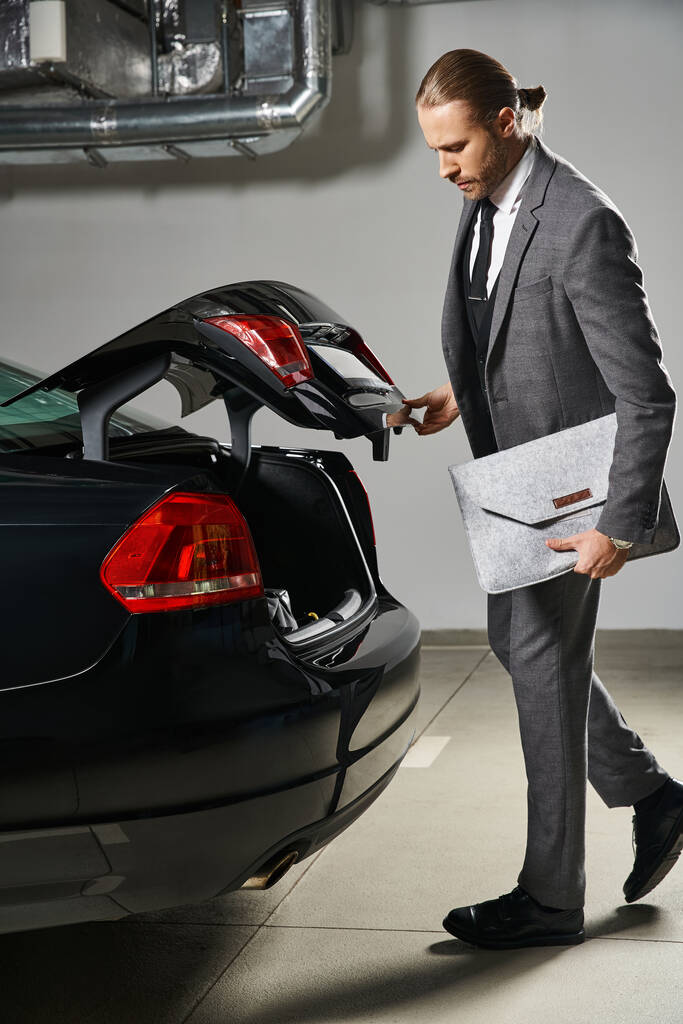 knappe roodharige man in elegante pak sluiten kofferbak van zijn auto op parkeerplaats, business concept - Foto, afbeelding