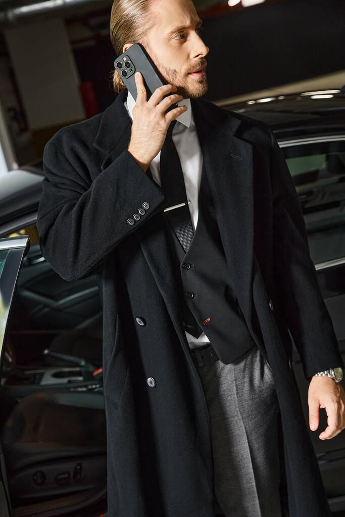 pohledný elegantní muž s culíkem a kravatou mluví telefonicky na parkovišti, obchodní koncept - Fotografie, Obrázek