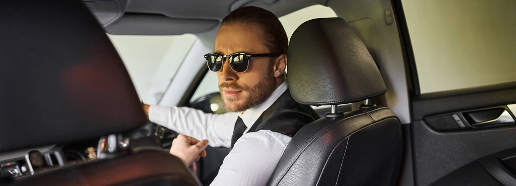 homme d'affaires attrayant avec des lunettes de soleil regardant la caméra tandis que derrière le volant, bannière - Photo, image