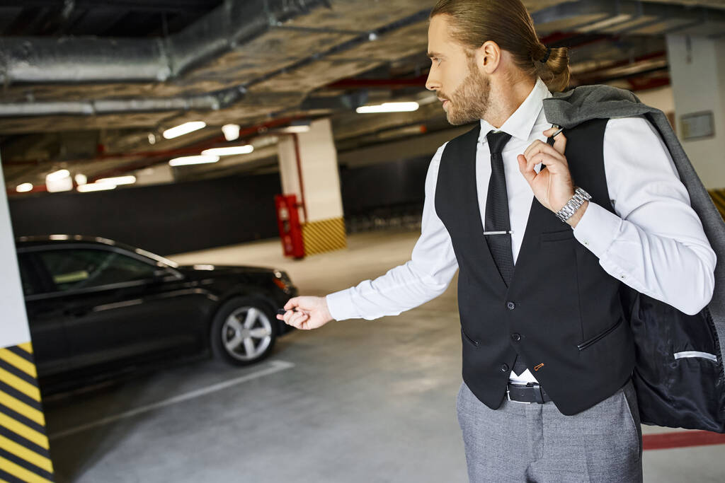 jóképű férfi szakállal fekete mellényben használja a kocsija kulcsát a parkolóban, üzleti koncepció - Fotó, kép