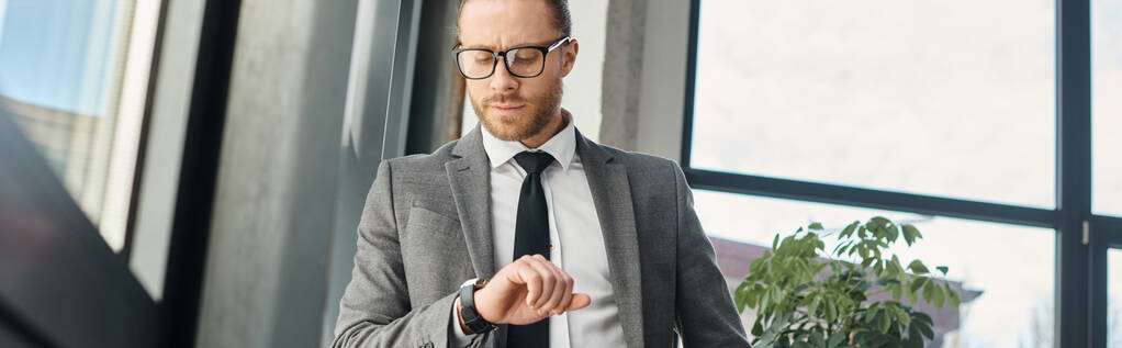 серьезный предприниматель в костюме и очках, глядя на наручные часы в офисе, горизонтальный баннер - Фото, изображение