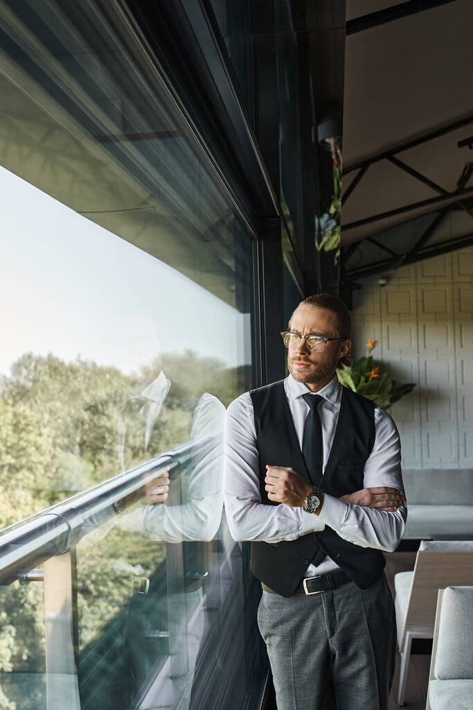 jóképű kifinomult üzletember okos fekete mellényben szemüveggel és nyakkendővel kinézve az ablakon - Fotó, kép