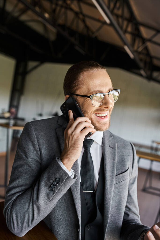joyeux homme d'affaires élégant en costume gris chic parlant activement par téléphone et souriant joyeusement - Photo, image