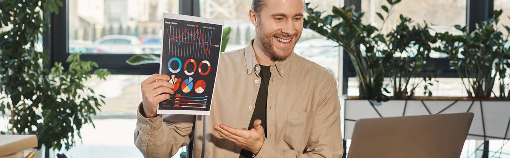Ofisteki dizüstü bilgisayardaki video görüşmesi sırasında bilgi grafikleri gösteren mutlu iş adamı, yatay afiş - Fotoğraf, Görsel