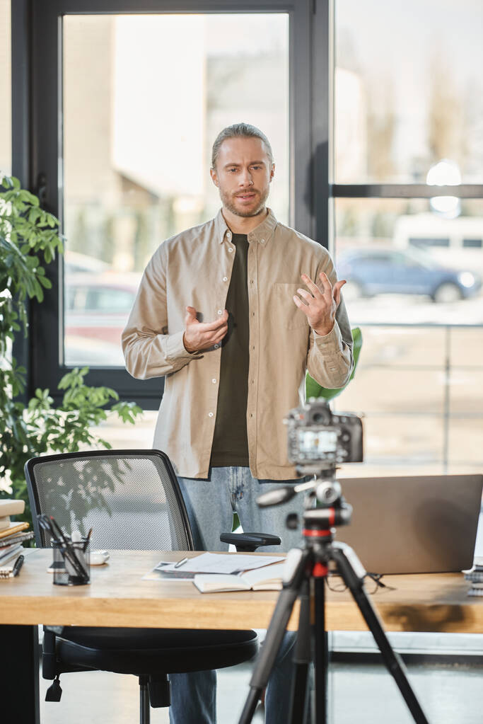 δημιουργικός επιχειρηματίας μιλώντας μπροστά από την ψηφιακή κάμερα κατά τη διάρκεια βίντεο blog στο γραφείο, μάρκετινγκ - Φωτογραφία, εικόνα