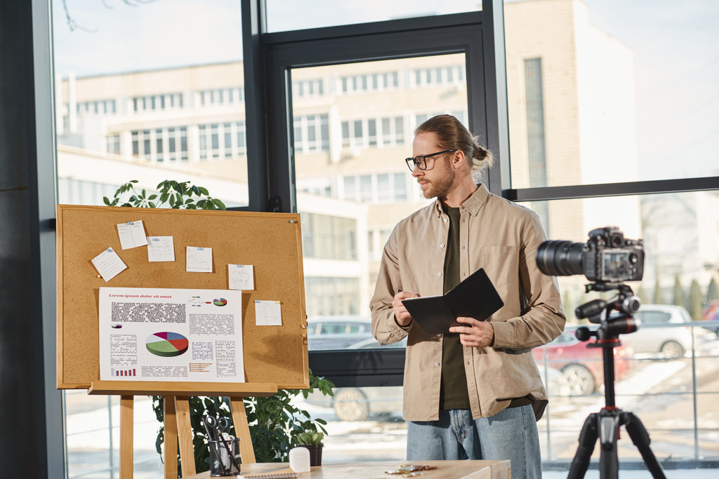 現代オフィスのビデオプレゼンテーション中にコルクボードでグラフを見ているノートを持つマネージャー - 写真・画像
