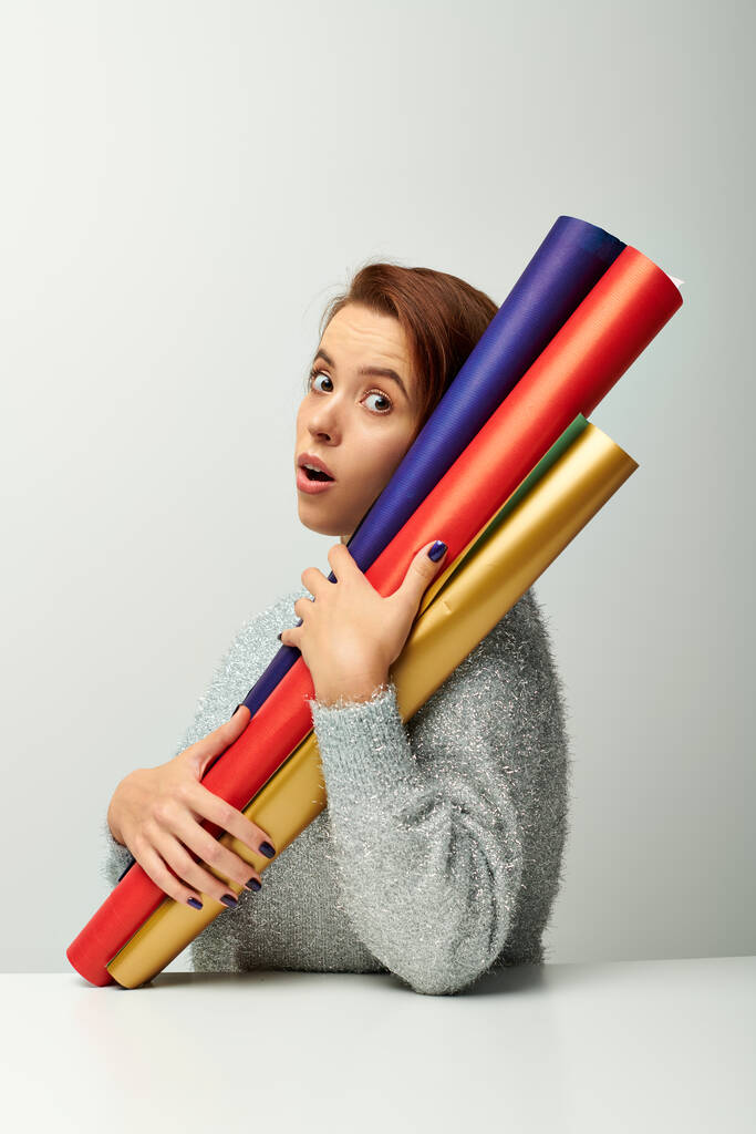 surprised woman with short hair holding colorful wrapping paper on grey backdrop, Christmas concept - Photo, Image