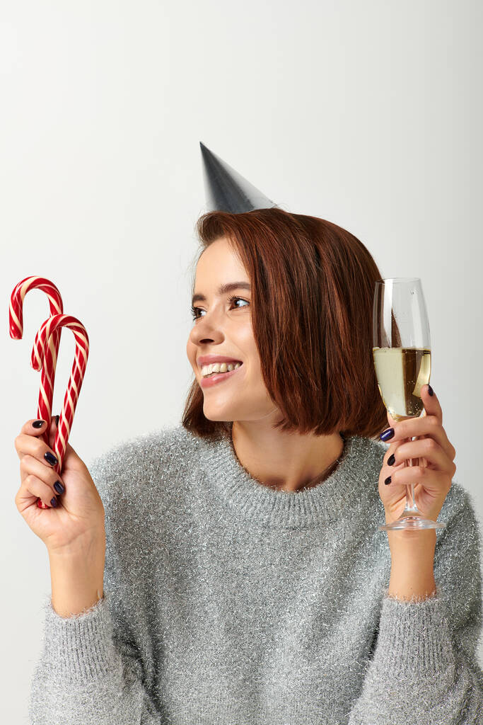 パーティーキャップの幸せな女性 シャンパングラスとキャンディー缶をグレーに保持, メリークリスマスコンセプト - 写真・画像
