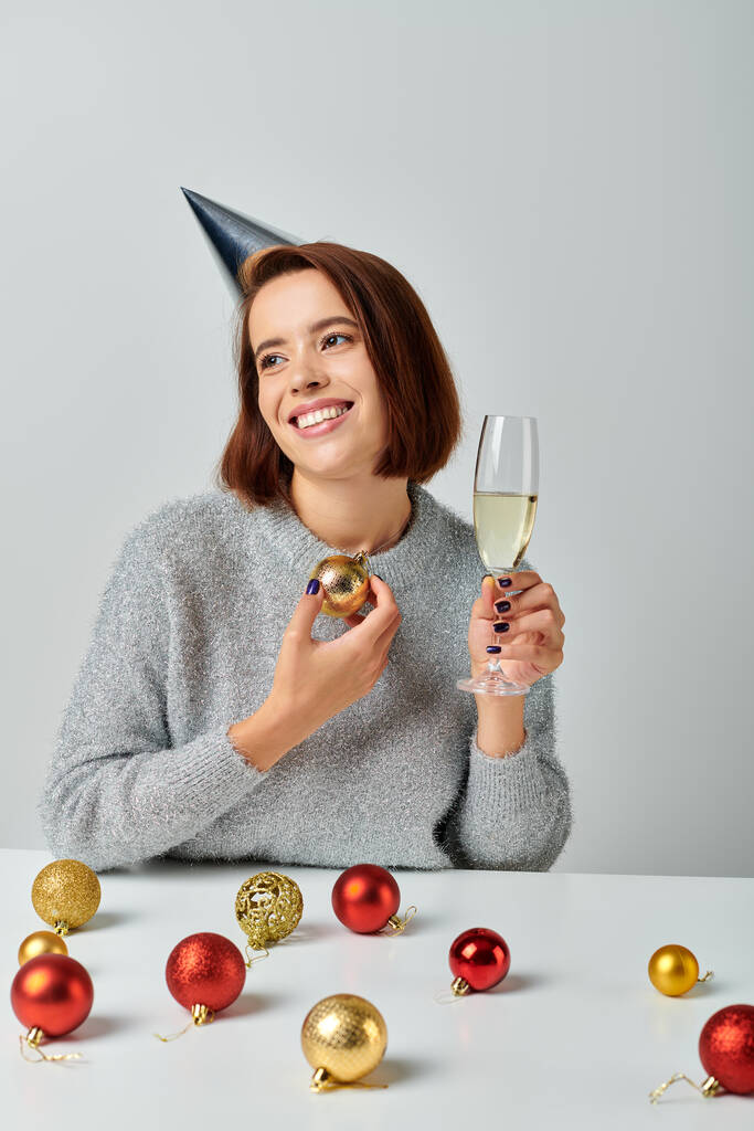 elégedett nő party sapkában kezében pezsgő üveg és csecsebecse szürke, Boldog Karácsonyt koncepció - Fotó, kép