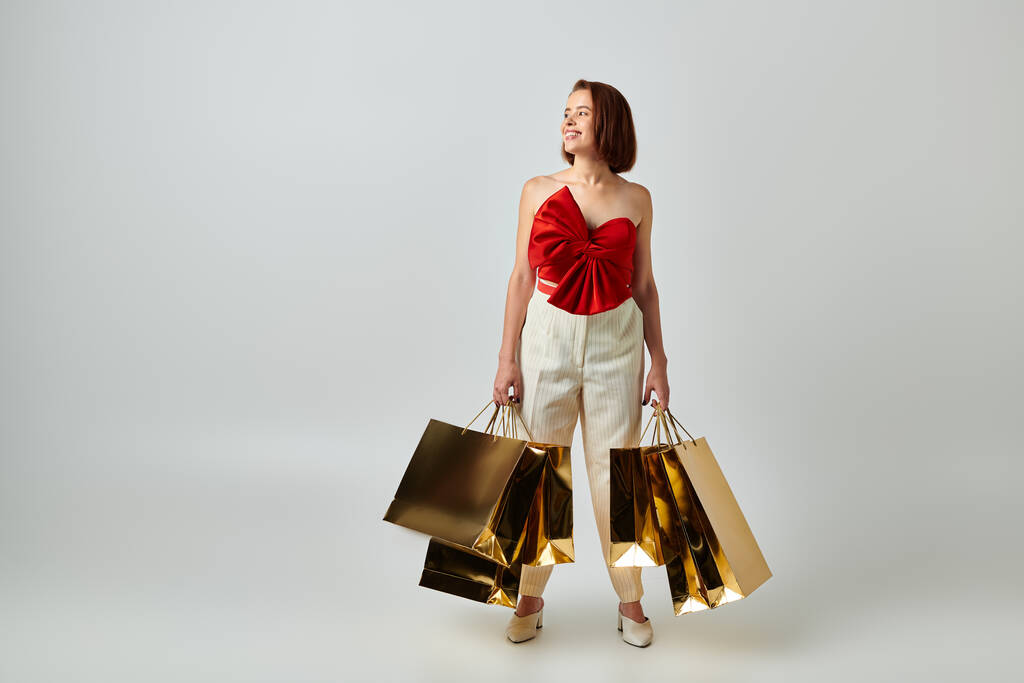 wakacje zakupy, szczęśliwa kobieta w modnym stroju trzyma torby na zakupy na szarym tle, Boże Narodzenie - Zdjęcie, obraz