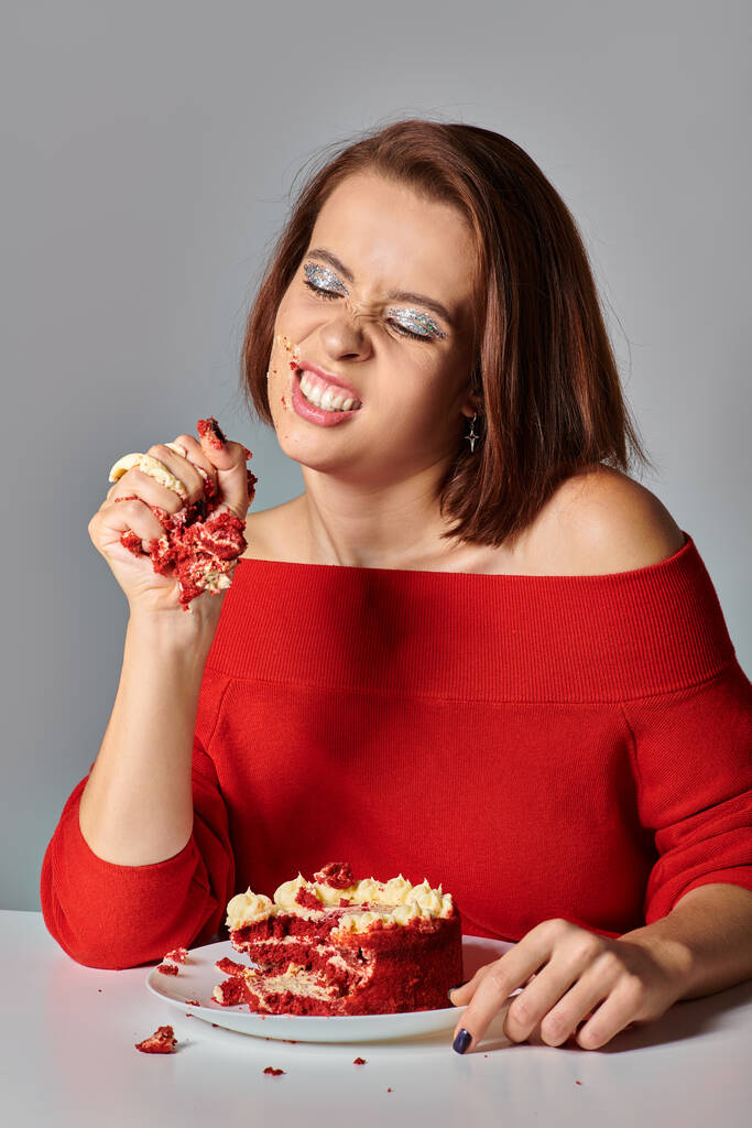 naštvaný narozeniny dívka v červeném oblečení rozbíjet lahodný kus narozeninového dortu na šedém pozadí - Fotografie, Obrázek